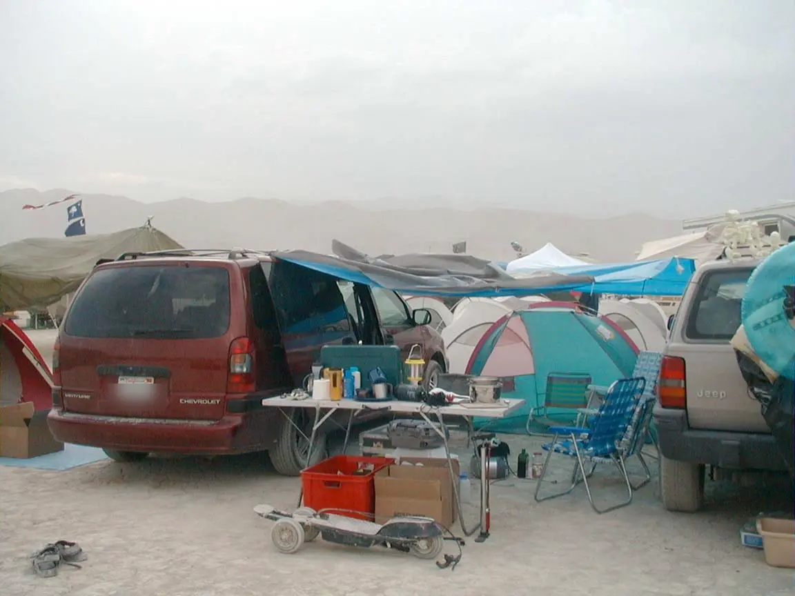 2002: the same van in a dust storm, a tarp off the roof rack shading the kitchen table